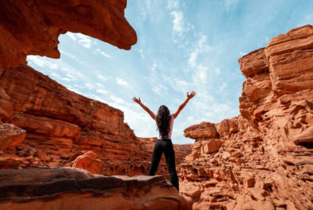 Woman raising her arms in a desert canyon under a bright blue sky