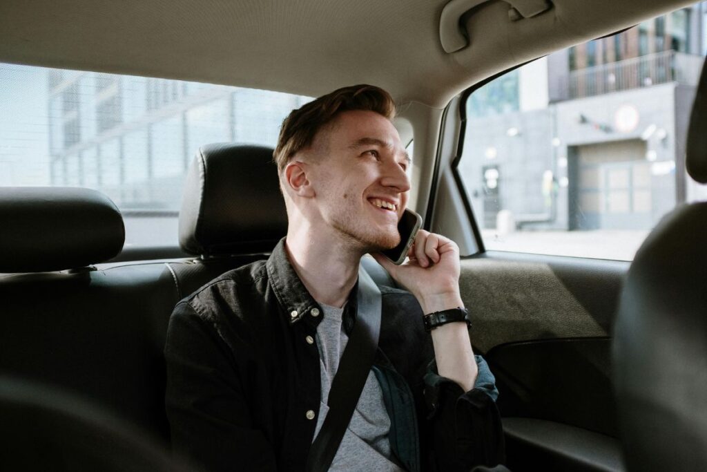 Man smiling while talking on the phone in the backseat of a car