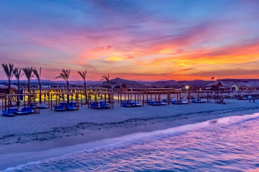 Sunset over a beach resort with palm trees and lounge chairs