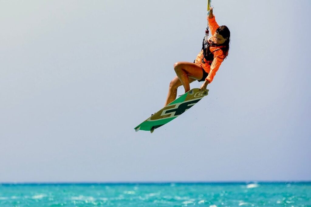 Woman mid-air while kiteboarding, showcasing thrilling water sports skills against a clear sky