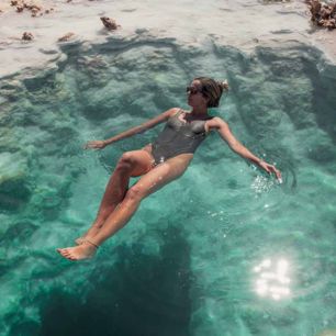 Woman floating peacefully in crystal-clear water, surrounded by rocks