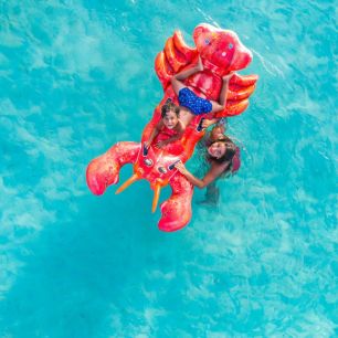 Two children on a large red lobster float enjoying the turquoise water
