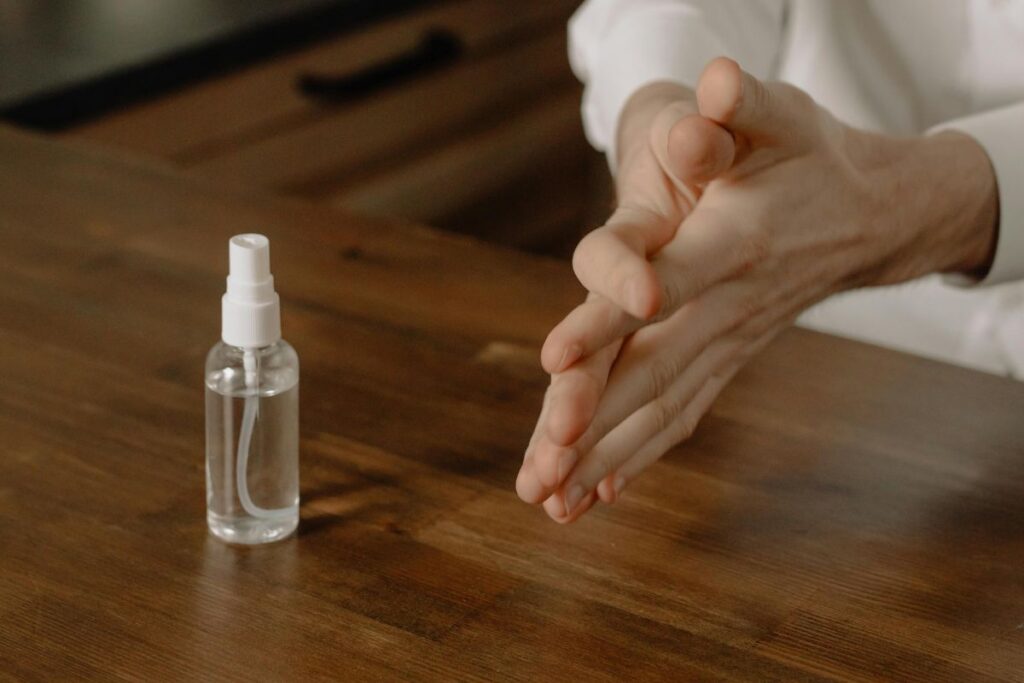 "Hands rubbing together beside a bottle of sanitizer on a table