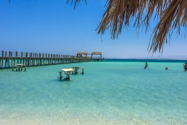 A shallow turquoise beach with a wooden pier and sunlit water tables