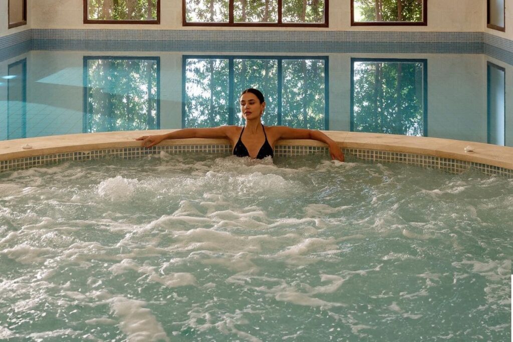 Woman relaxing in an indoor jacuzzi with large arched windows in the background