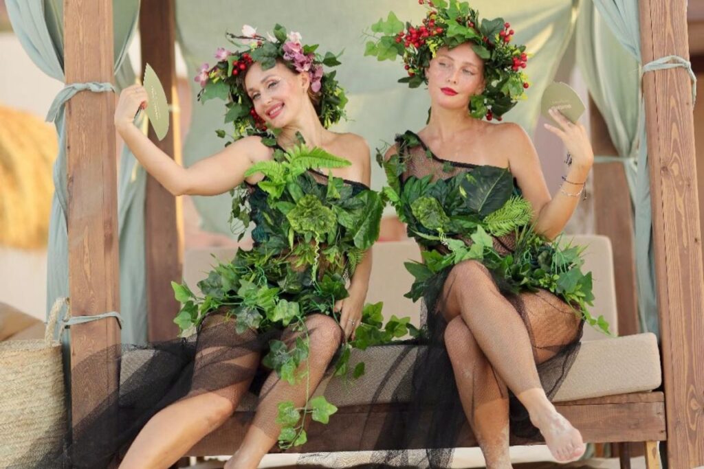 Two women in nature-inspired costumes adorned with leaves and flowers, posing for a whimsical photo