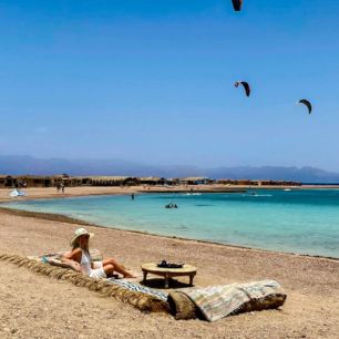Woman relaxing on a beach, watching kite surfers in the sky over the turquoise sea