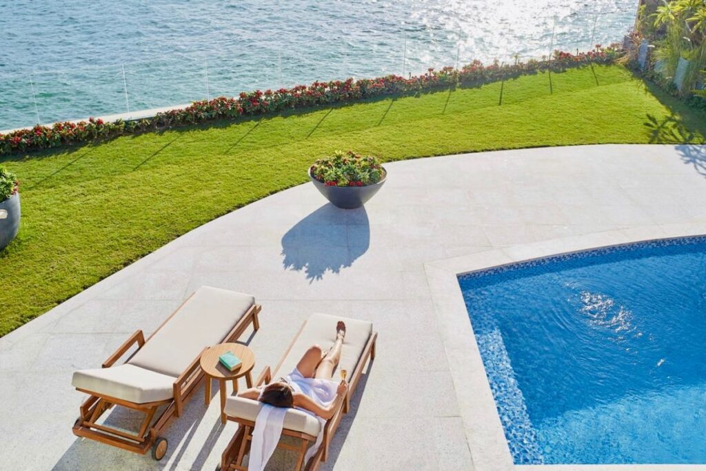 A luxurious poolside view overlooking a calm ocean with green lawns and flowers