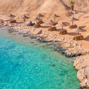 A secluded sandy beach with straw umbrellas and lounge chairs, overlooking a clear turquoise sea